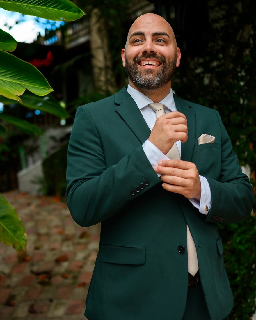 Daniel Velez, founder of Smile NOLA, in a forest-green suit and cream tie photographed in a tropical garden courtyard